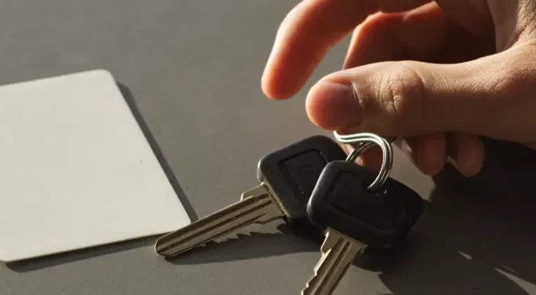 Een hand met autosleutels op een tafel, naast een blanco pasje.